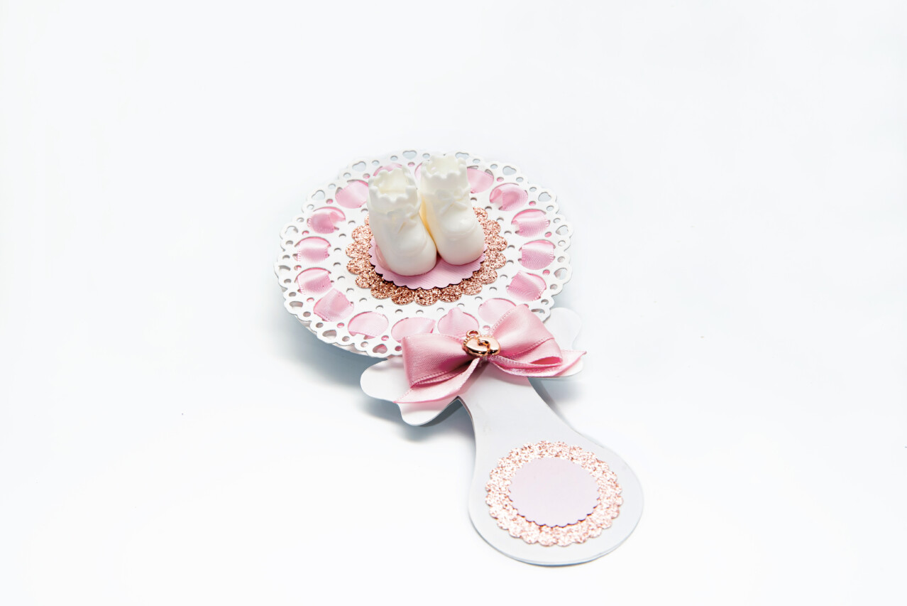 Baby girl shower rattle party favor with baby shoes and pink ribbon on decorated table