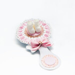 Baby girl shower rattle party favor with baby shoes and pink ribbon on decorated table