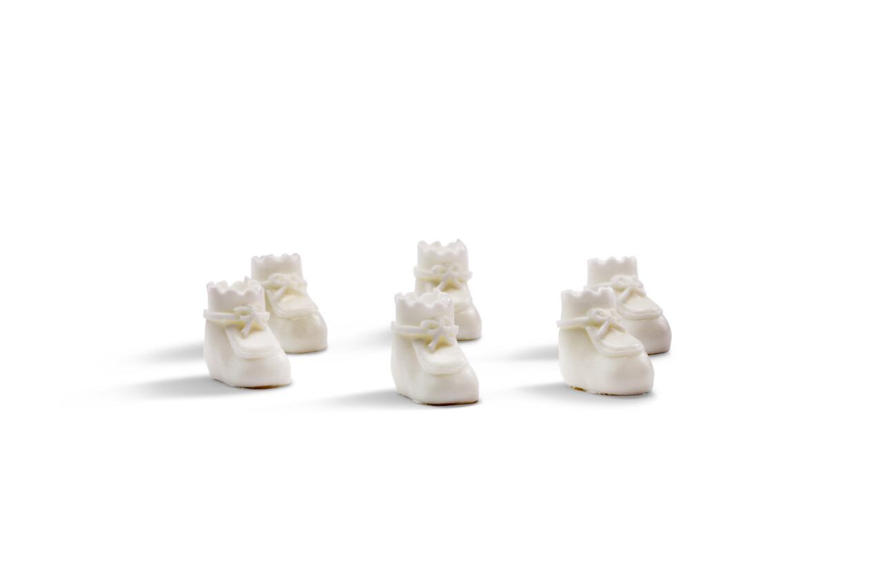 Mini white baby shoes for baby shower crafts and DIY party decorations on pink backdrop