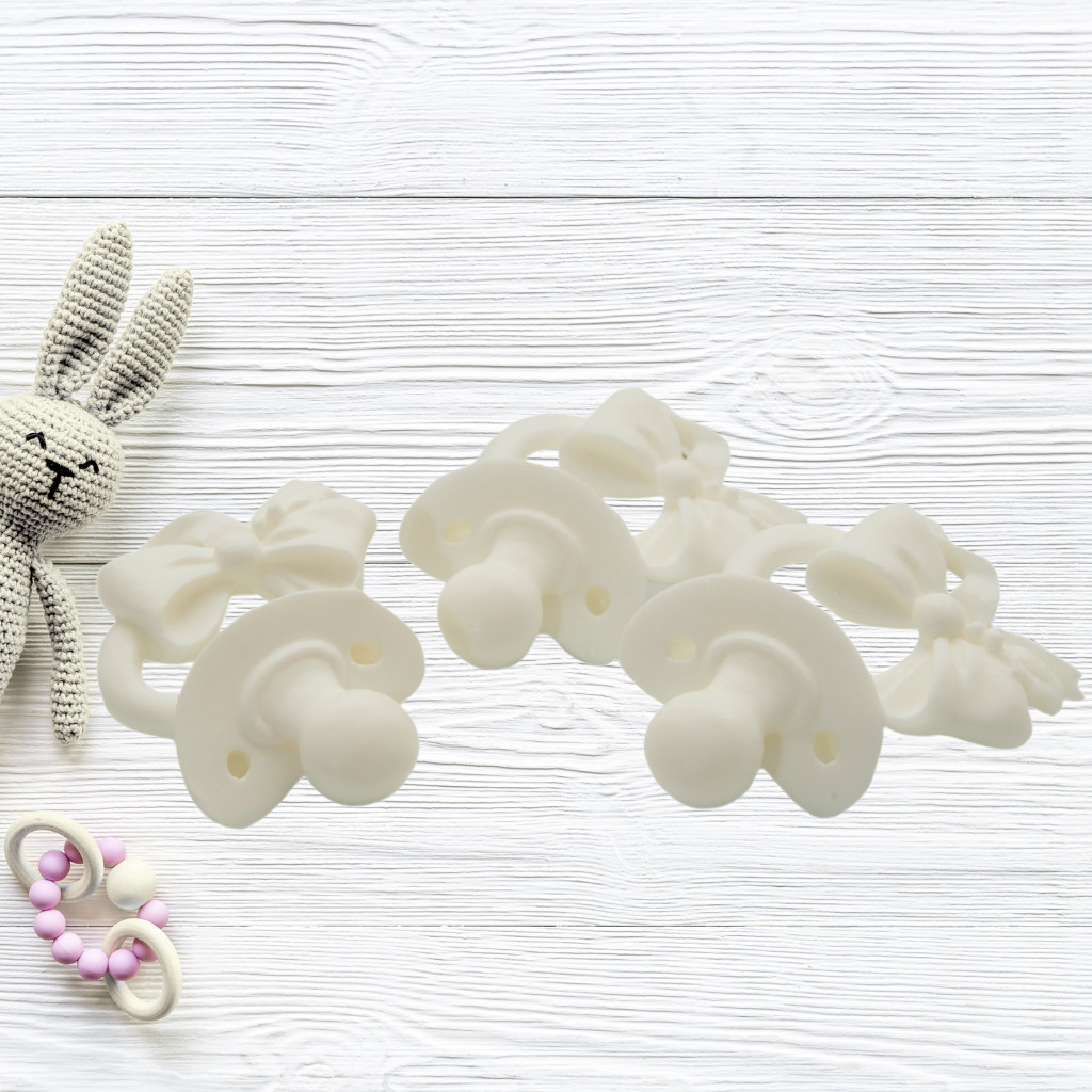 DIY baby shower pacifier decorations set with six white resin pacifiers on wooden background
